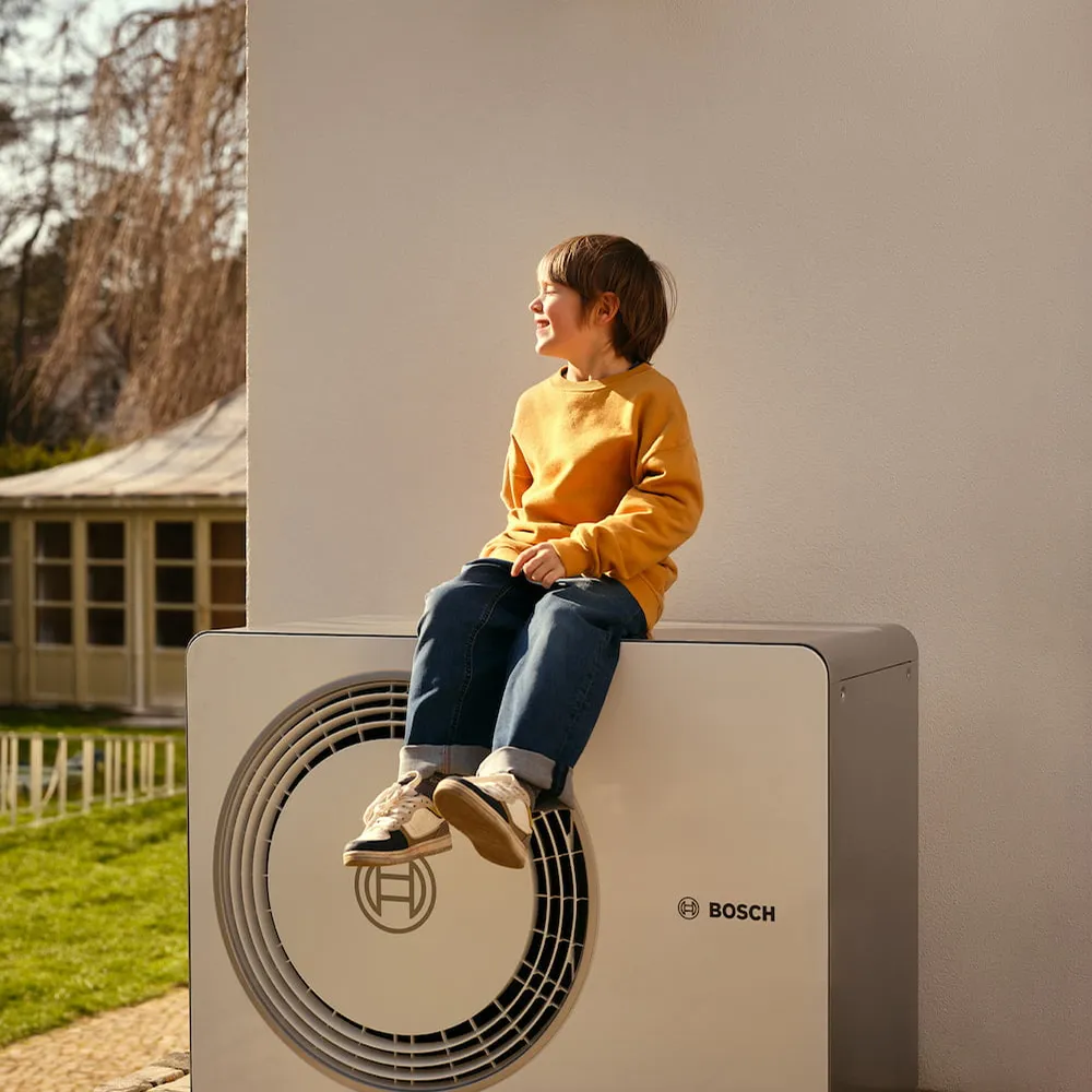 Junge sitzt auf Infravoltaic Wärmepumpe vor einer Hauswand